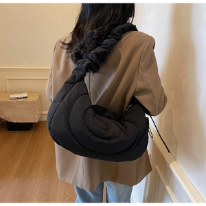 Close-up of a black quilted puffy crescent bag worn by a model in a minimalist room