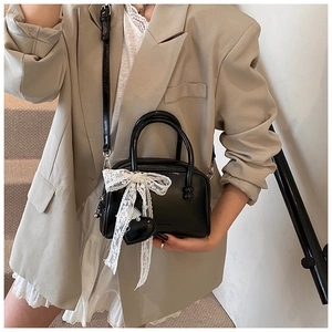 Model wearing black glossy bowling bag with large lace bow and heart charm