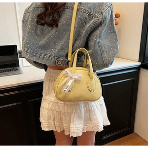 Detail of a creamy yellow top handle bag with a silk bow and lychee texture