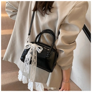 Détail du sac bowling noir avec nœud en dentelle blanche sur une tenue beige