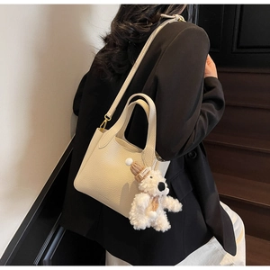 Detail view of cream lychee pattern leather bucket bag with cute plush bear charm
