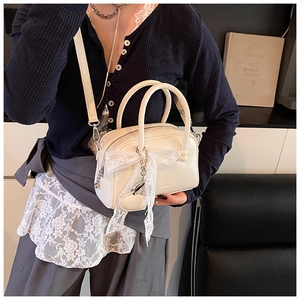 Detail of cream white leather handbag with lace bow and heart-shaped pendant charm