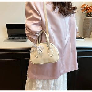 Chic cream bowling bag with ribbon detail shown as a shoulder bag on an elegant model