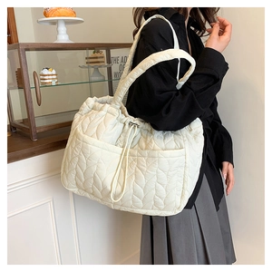 Close-up of cream quilted shoulder bag with leaf pattern and drawstring detail on model