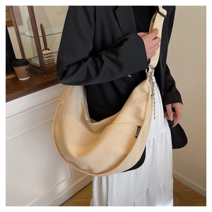 Detail of minimalist beige canvas crescent bag with black brand tag and wide strap