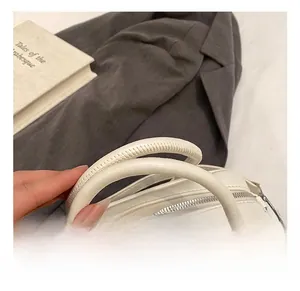 Détail de la poignée en cuir blanc avec coutures fines sur un sac bowling minimaliste