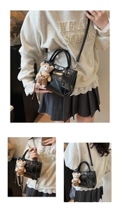 Detail view of glossy black faux leather crossbody bag with silver twist lock and bear charm