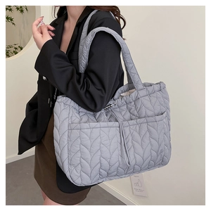 Macro detail of quilted wave stitching and drawstring pocket on light gray tote bag
