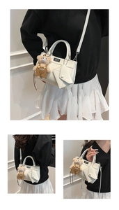 Detail of white PU leather handbag featuring a metal lock, small pouch, and bear charm