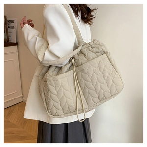 Close-up of beige quilted tote bag with leaf texture and side drawstring detail