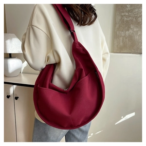 Detail of burgundy canvas crossbody bag showing a wide strap and side woven label