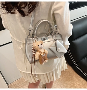 Détail d'un sac bandoulière argenté avec pendentif ours et fermoir rotatif chic