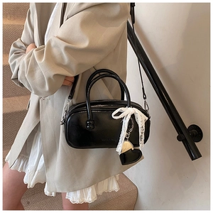 Close-up of black glossy handbag featuring white lace bow and heart metal charm detail