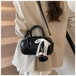 Detail of black glossy handbag with white lace bow and heart charm on a round handle