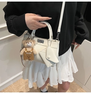 Detail of white leather handbag featuring silver lock, plush bear charm, and envelope pouch