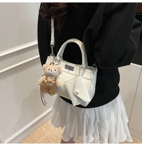 Détail d'un sac bandoulière blanc minimaliste avec fermoir rotatif et charm ourson