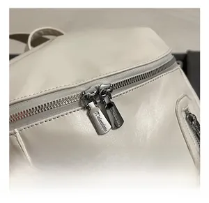 Close-up of dual silver metal zippers and refined leather texture on the white backpack