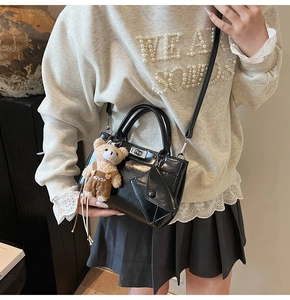 Detail of black glossy handbag with silver lock, teddy bear charm and mini pouch