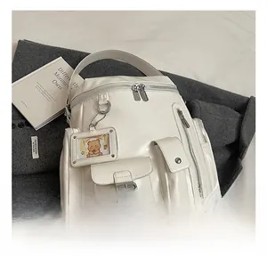 Close-up of ivory PU leather backpack details featuring buckle pockets and bear charm