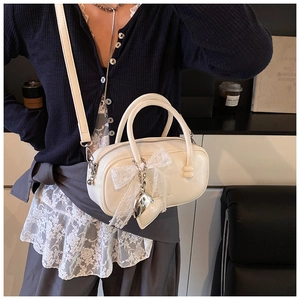 Detail view of the elegant cream bowling bag featuring a sweet lace bow and metal heart charm.
