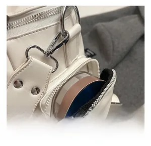 Detailed close-up of white PU leather backpack featuring silver hooks and zipper pockets