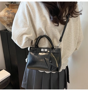 Detail view of glossy black PU leather handbag with silver turn-lock and mini pouch charm