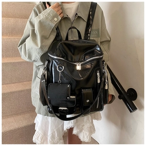 Detail view of a glossy black backpack with multiple silver zippers on a model