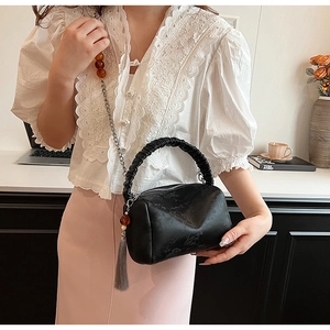Close-up of black pleated handle handbag with chain strap and fringe tassel charm