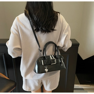 Détail du sac bowling en cuir verni noir avec breloque cœur porté par un mannequin