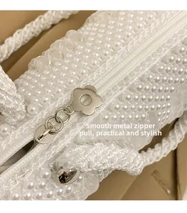 Detail of white pearl beaded bag featuring a flower shaped silver metal zipper puller