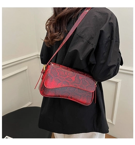 Close-up of red snake print faux leather shoulder bag worn by a model in a minimalist setting