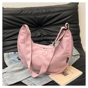 Detail showing the light pink canvas half-moon bag with adjustable strap on a sofa