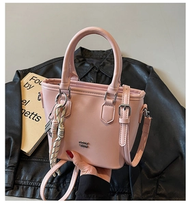 Gros plan détaillé du sac seau en cuir rose avec logo argenté et pendentif tissé