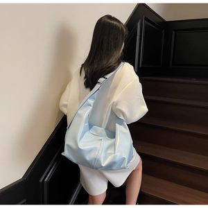 Détail du sac demi-lune bleu clair brillant porté par un mannequin dans un cadre moderne