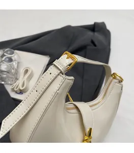Detail view of cream white crescent bag showing adjustable strap and gold metal zipper