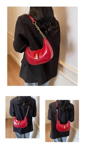 Detail view of red crescent shoulder bag with golden chain and metallic buckle closure