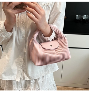 Pink pleated shoulder bag with magnetic metal clasp held by a model in a casual setting