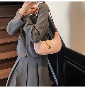 Pink crescent underarm bag shown on a model featuring glossy finish and gold metal buckle