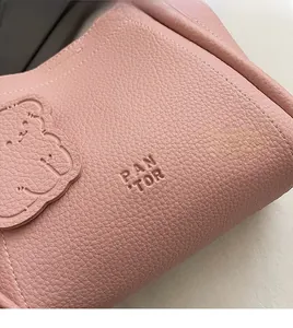 Close-up of pink lychee grain leather handbag with embossed bear motif and brand text