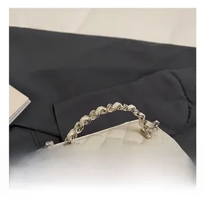 Detail of white quilted handbag with metallic chain handle and faux pearl accents