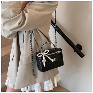 Detail of black quilted crossbody bag with pearl bow and silver heart pendant decoration