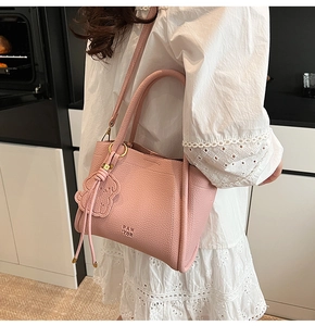 Detail of pink lychee leather handbag with bear charm and detachable strap on model