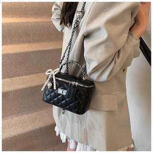 Close-up of quilted black crossbody bag with pearl bow and heart pendant on a model