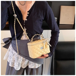 Detail of light yellow quilted vanity bag with metal chain strap and pearl bow charm