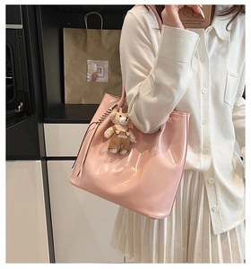 Detail of pink glossy leather tote bag with plush bear charm and woven texture handle