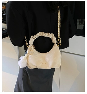 Detail of off-white pleated dumpling bag with metal chain and plush charm on black blazer