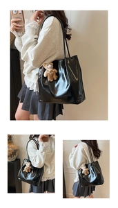 Detail of glossy black tote bag with long shoulder straps and a cute brown bear charm