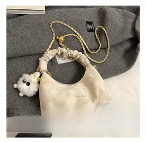 Detail of off-white pleated dumpling bag with golden chain strap and plush charm