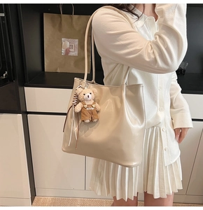 Detail of cream leather tote bag with cute teddy bear charm and large shoulder strap