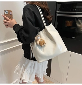 Detailed side view of cream white tote bag with bear charm and tassel on model
